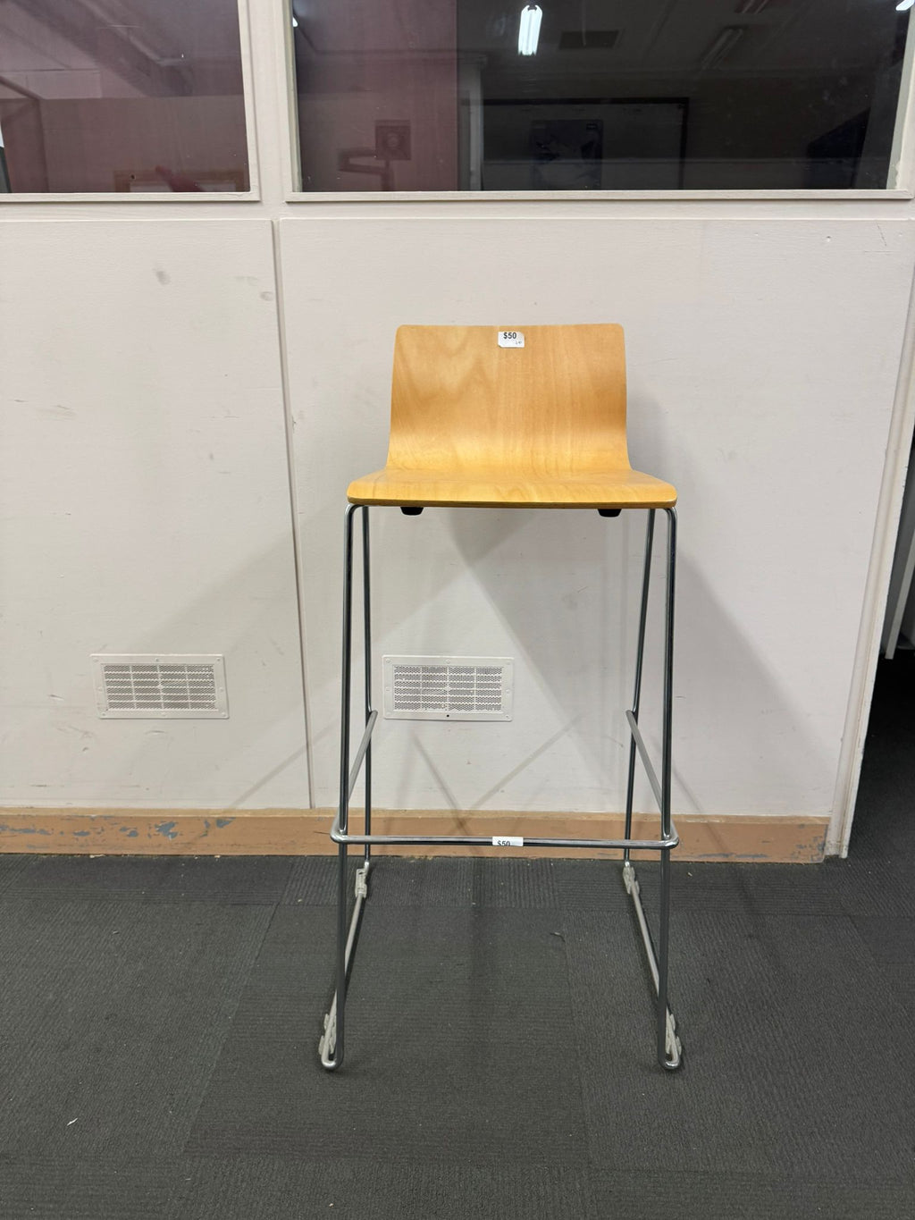 Wooden bar stool with metal legs against a white wall.