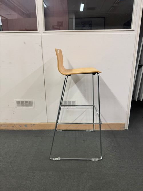 Bar stool with wooden seat and metal frame on a gray floor.