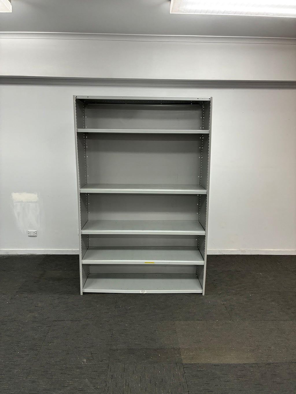 A gray metal wall-mounted shelving unit with five open cubby compartments, shown against a white wall and dark gray carpet.