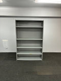 A gray metal wall-mounted shelving unit with five open cubby compartments, shown against a white wall and dark gray carpet.
