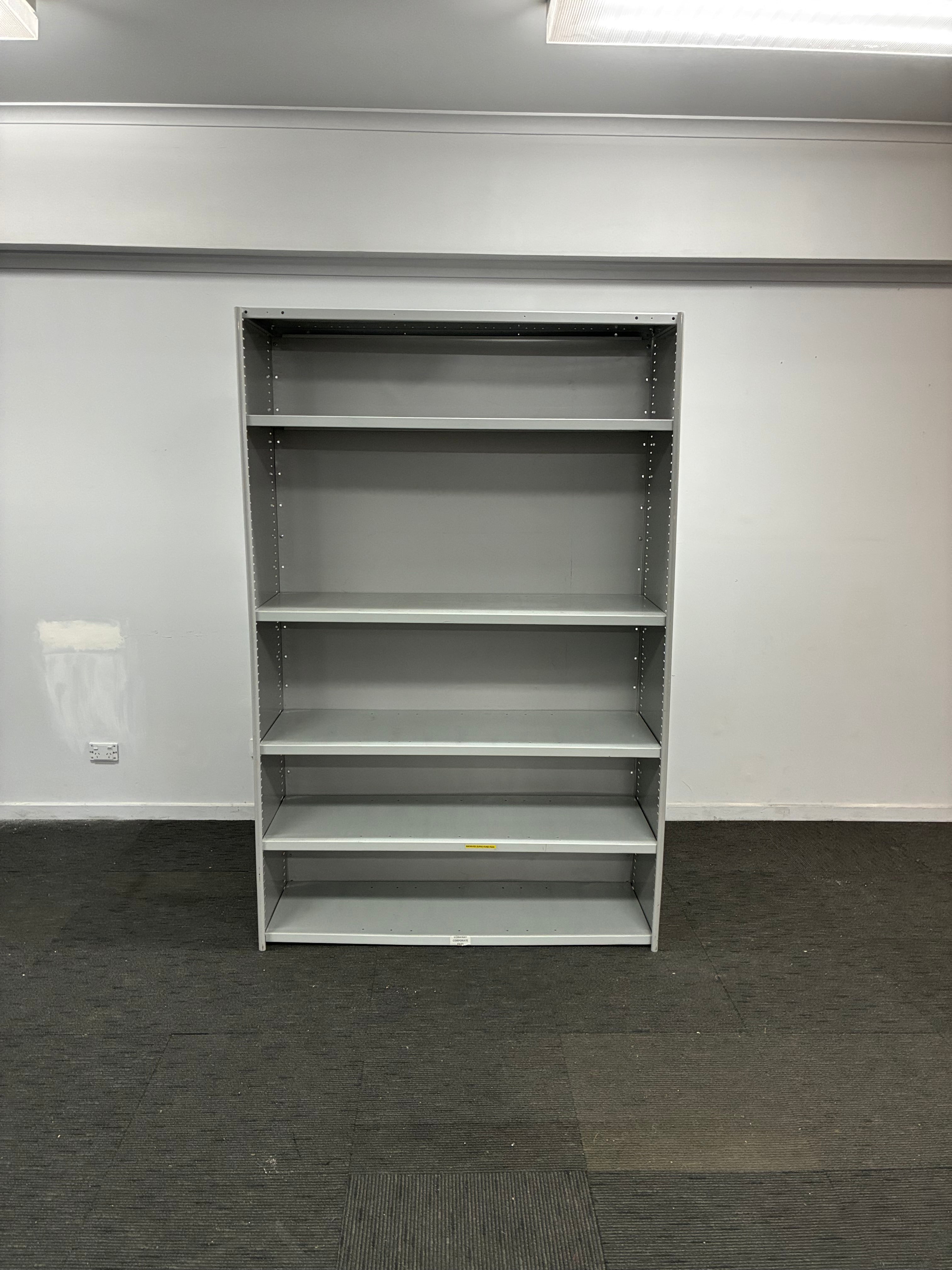 A gray metal wall-mounted shelving unit with five open cubby compartments, shown against a white wall and dark gray carpet.