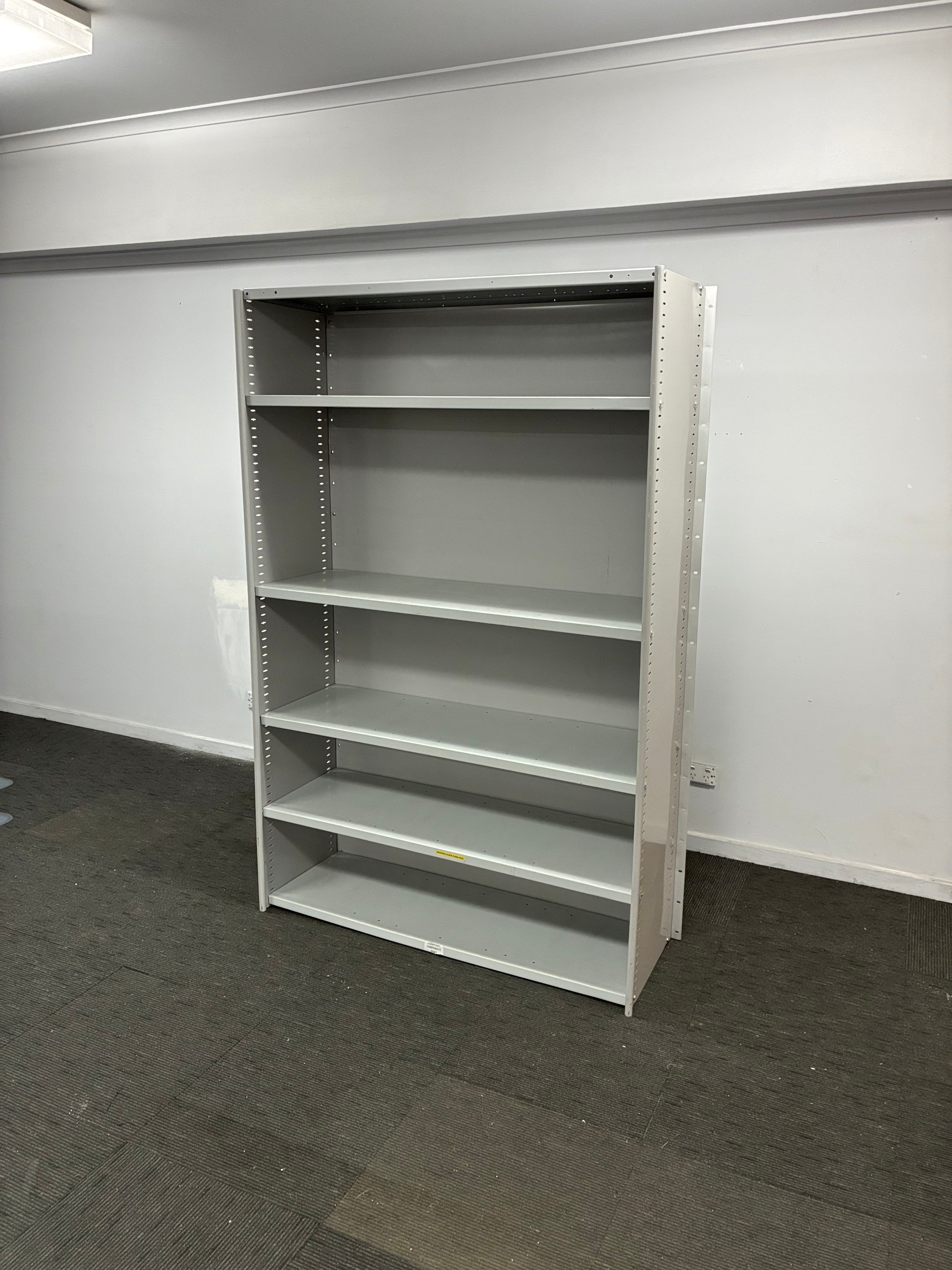 A gray metal wall-mounted organizer shelf with five vertical compartments, shown against a white wall and dark gray floor.