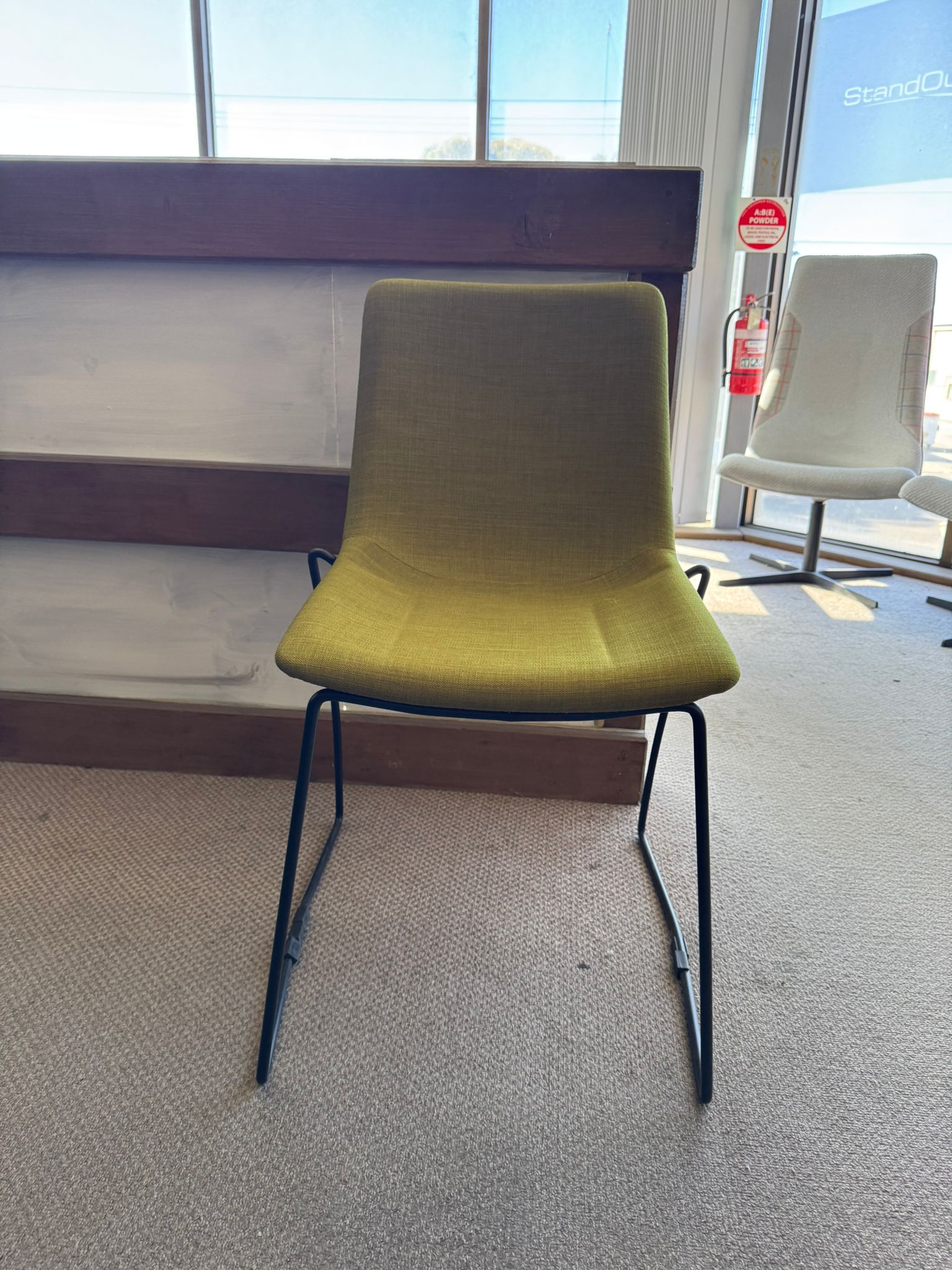 Green chair in a room with large windows and a fire extinguisher visible.