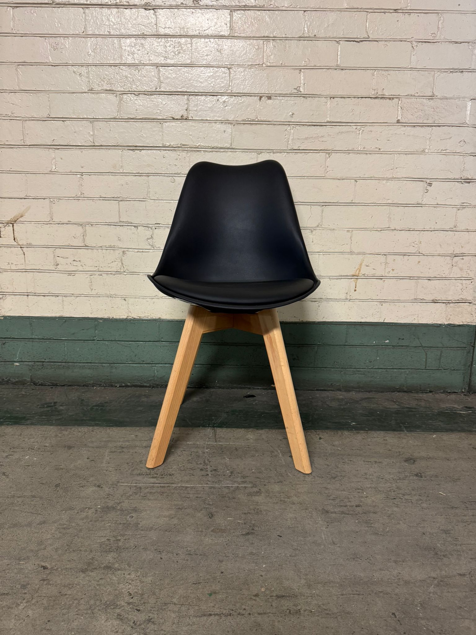 Black chair with wooden legs against a brick wall.