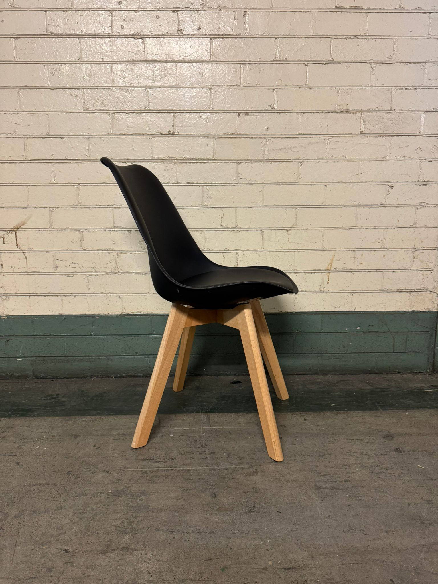 Black chair with wooden legs against a brick wall.