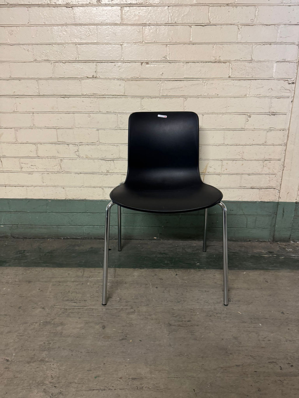 Black chair with chrome legs against a light brick wall.