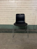 Black chair with chrome legs against a light brick wall.