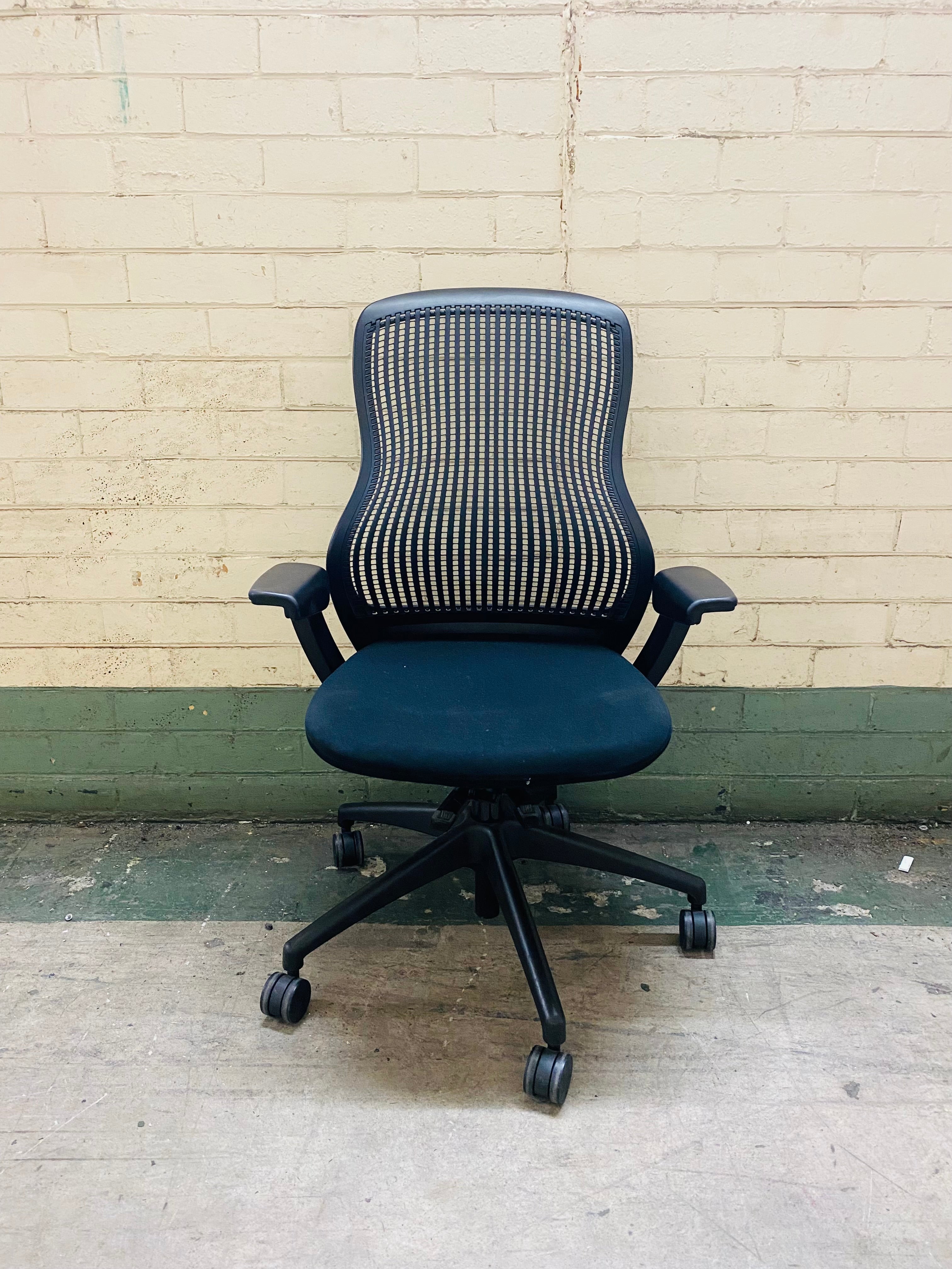 Blue office chair with mesh back against a beige brick wall.