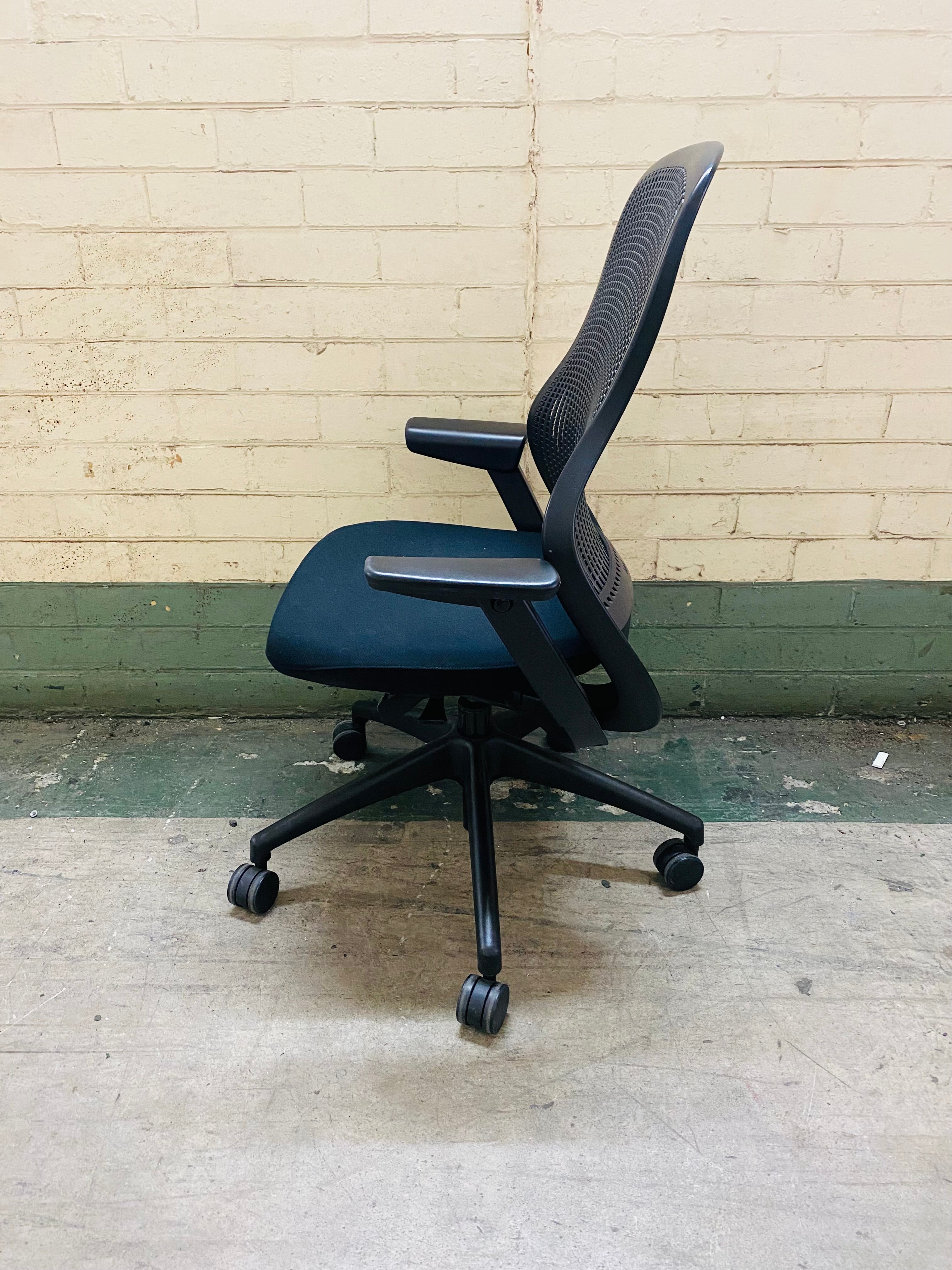 Blue office chair with black mesh backrest against a brick wall.