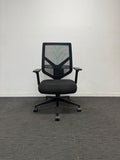 A black mesh office chair with a five-star wheeled base, positioned against a plain white wall on a gray textured carpet.