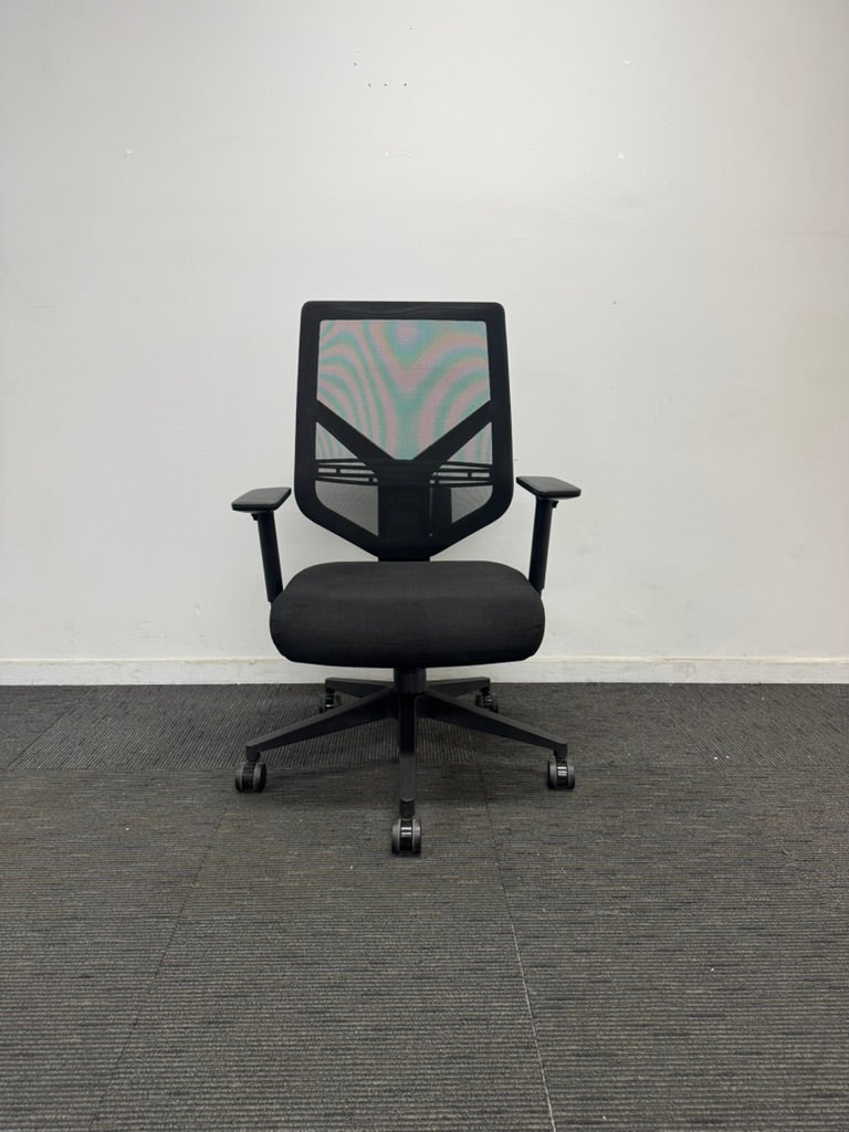 A black mesh office chair with a five-star wheeled base, positioned against a plain white wall on a gray textured carpet.