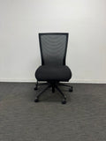 A black mesh office chair with a five-star wheeled base, positioned against a plain white wall on a gray carpeted floor.