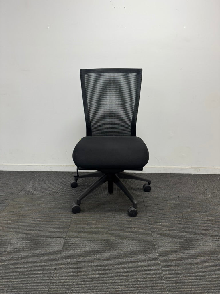A black mesh office chair with a five-star wheeled base, positioned against a plain white wall on a gray carpeted floor.