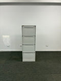 A four-drawer white metal file cabinet or storage unit mounted against a white wall, with a dark gray floor visible on the right side.