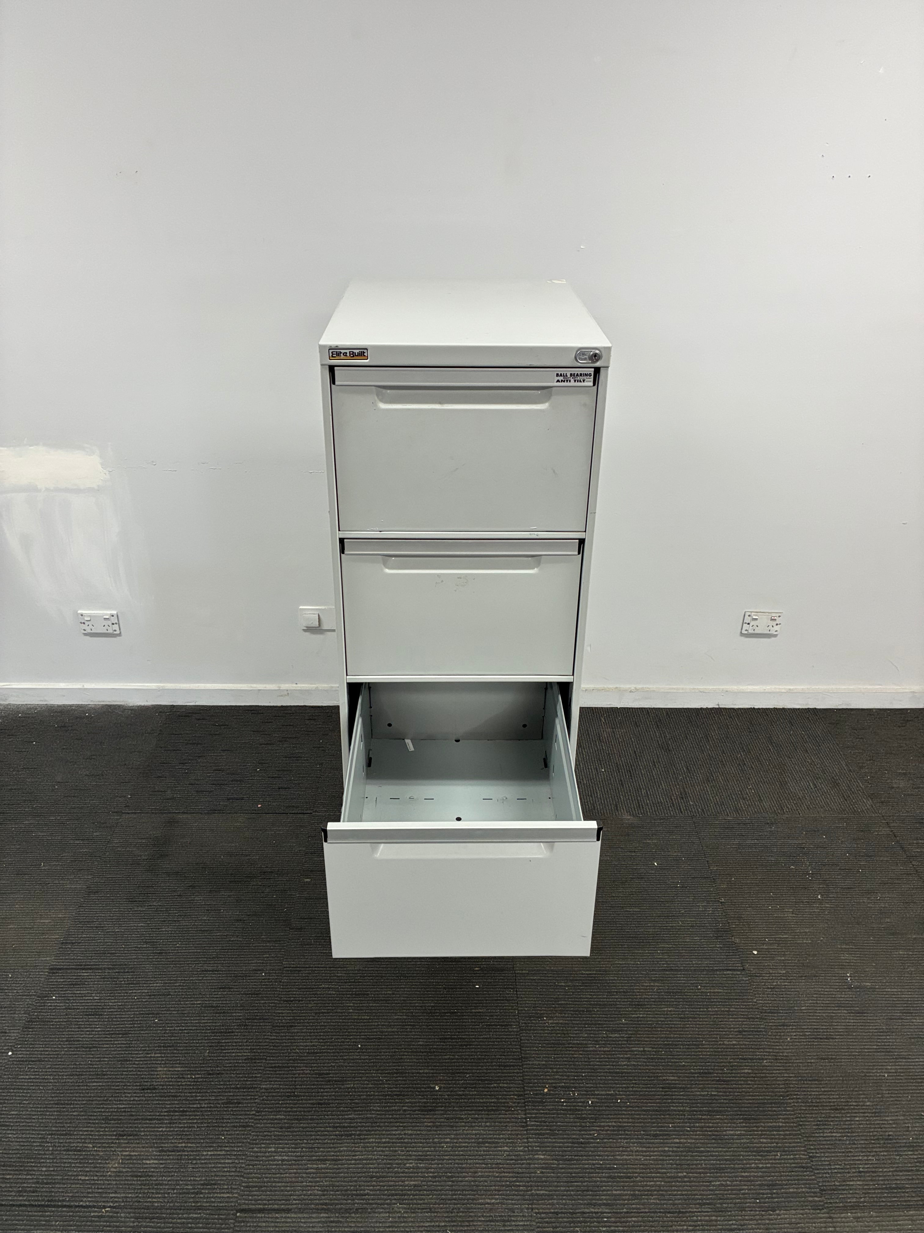 A white metal two-drawer filing cabinet with one drawer open, shown against a white wall and dark gray carpeted floor.