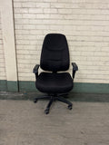 Black office chair against a light brick wall.