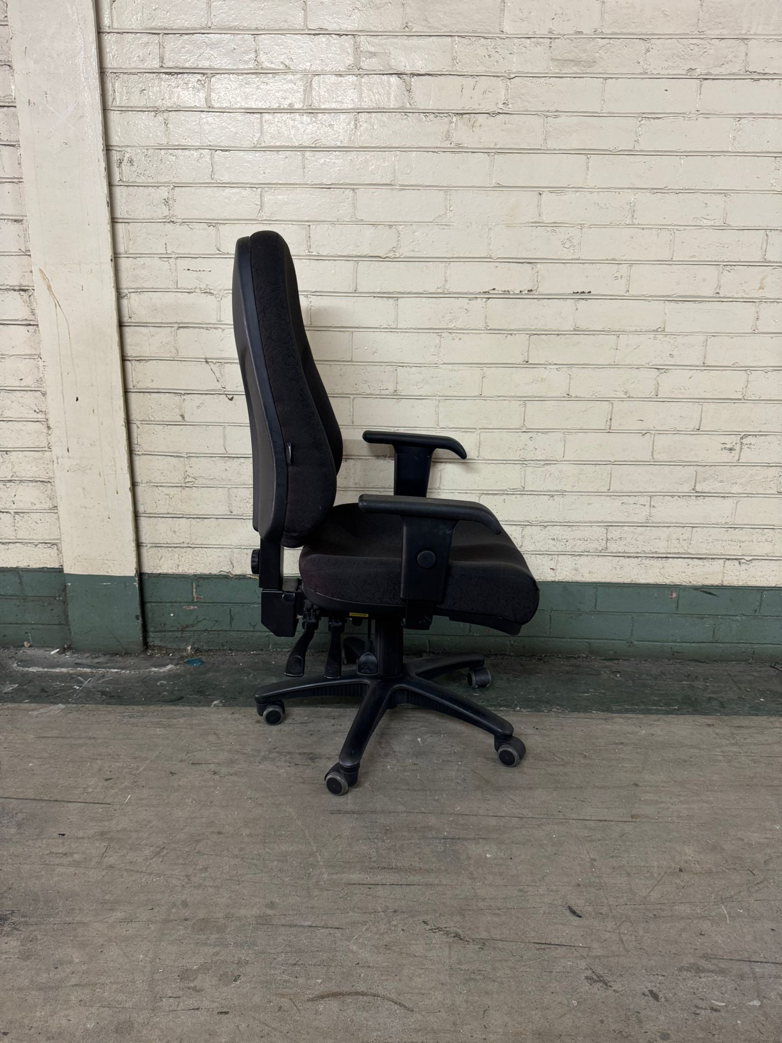 Black office chair against a white brick wall.