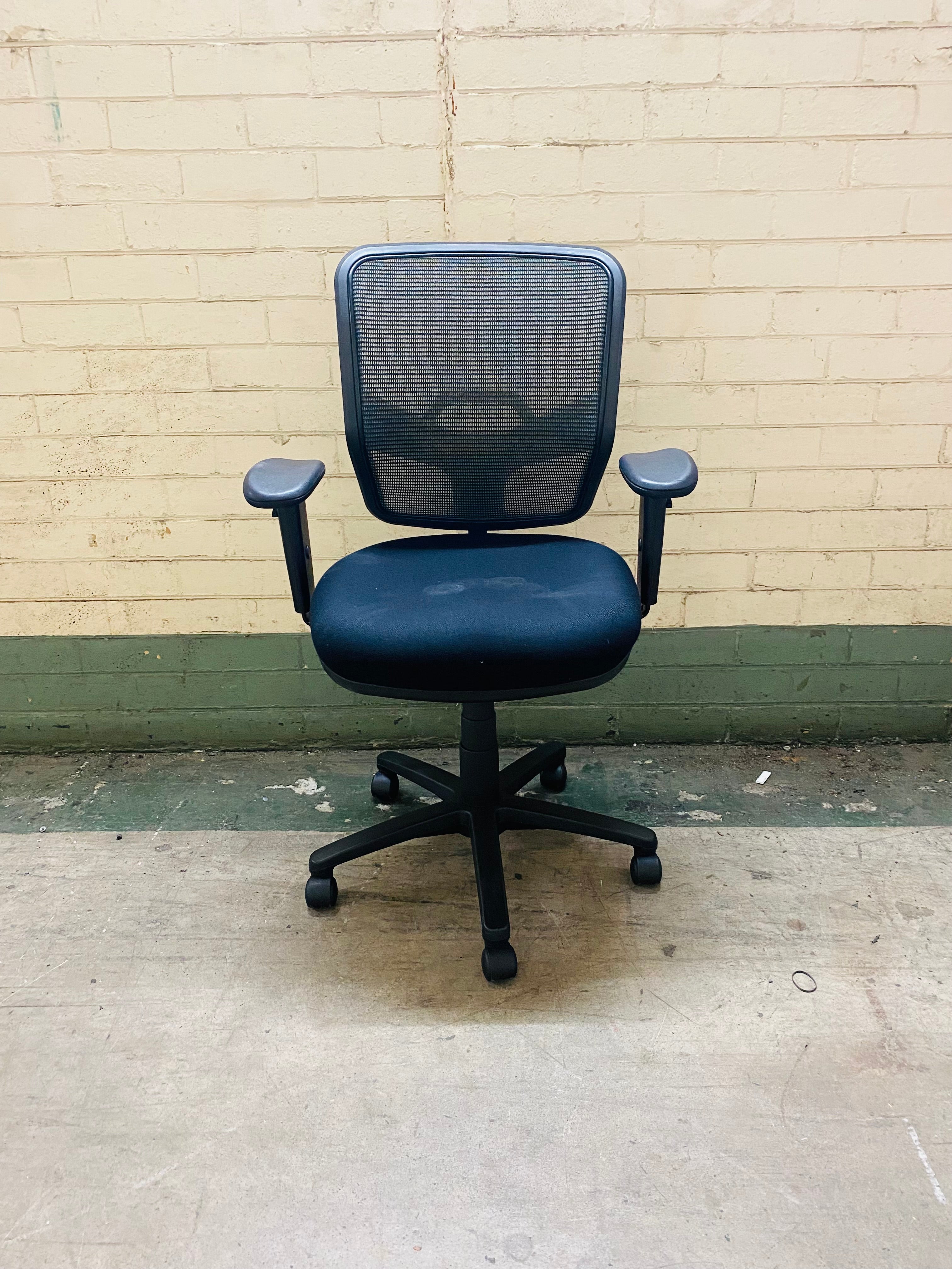 Blue office chair against a beige brick wall.