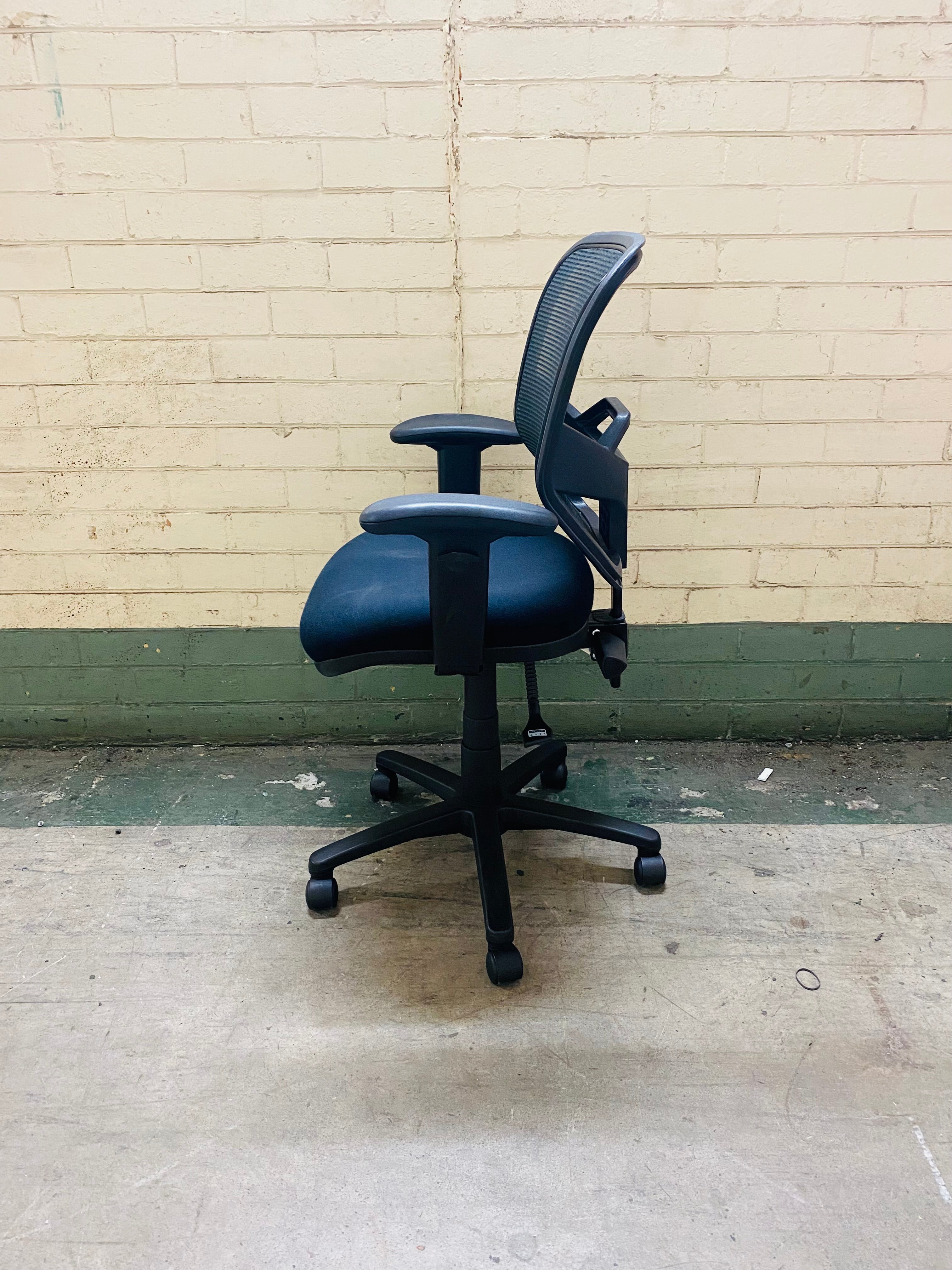 Black office chair against a beige brick wall.