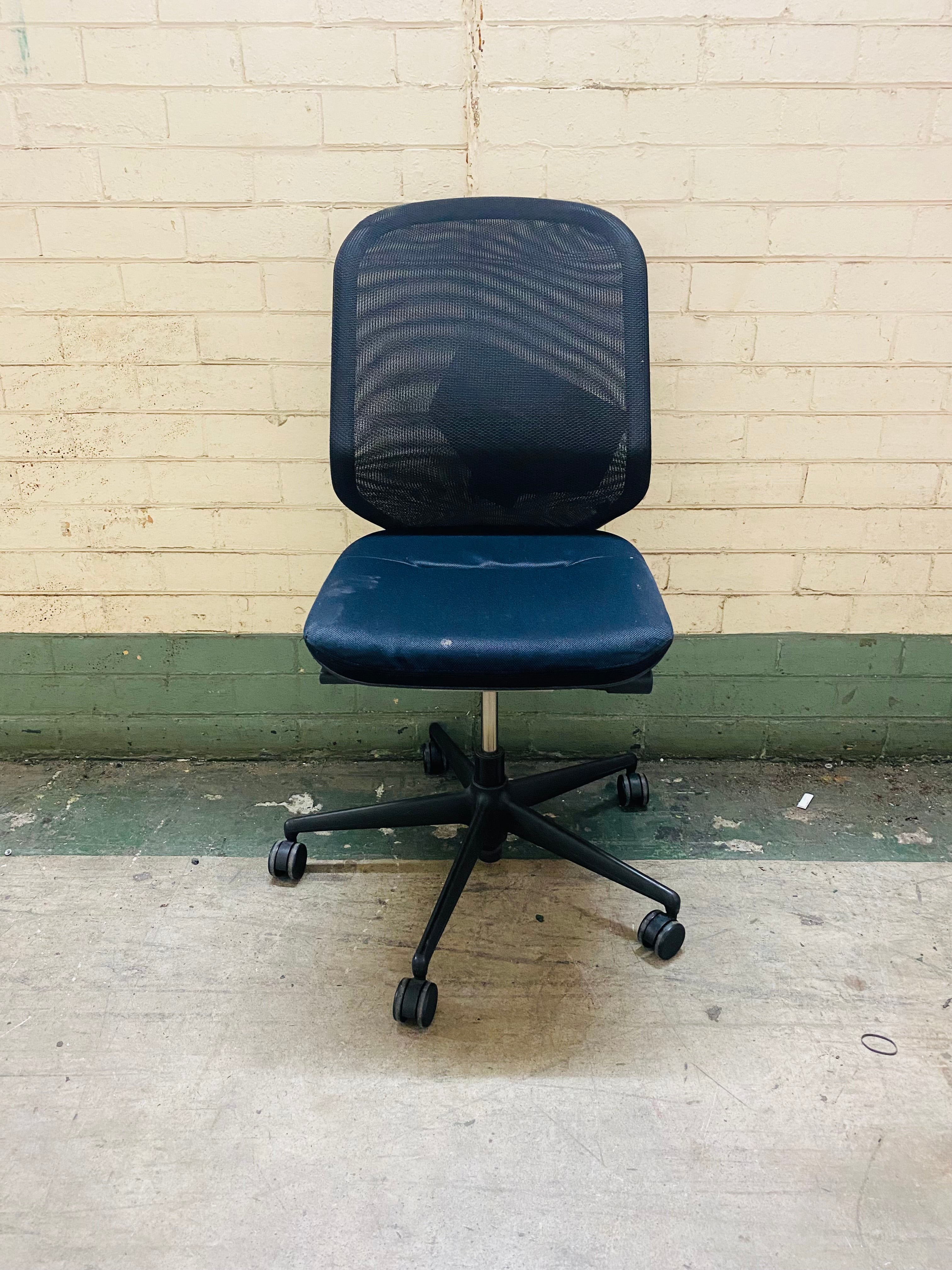 Blue office chair with mesh backrest against a beige brick wall.
