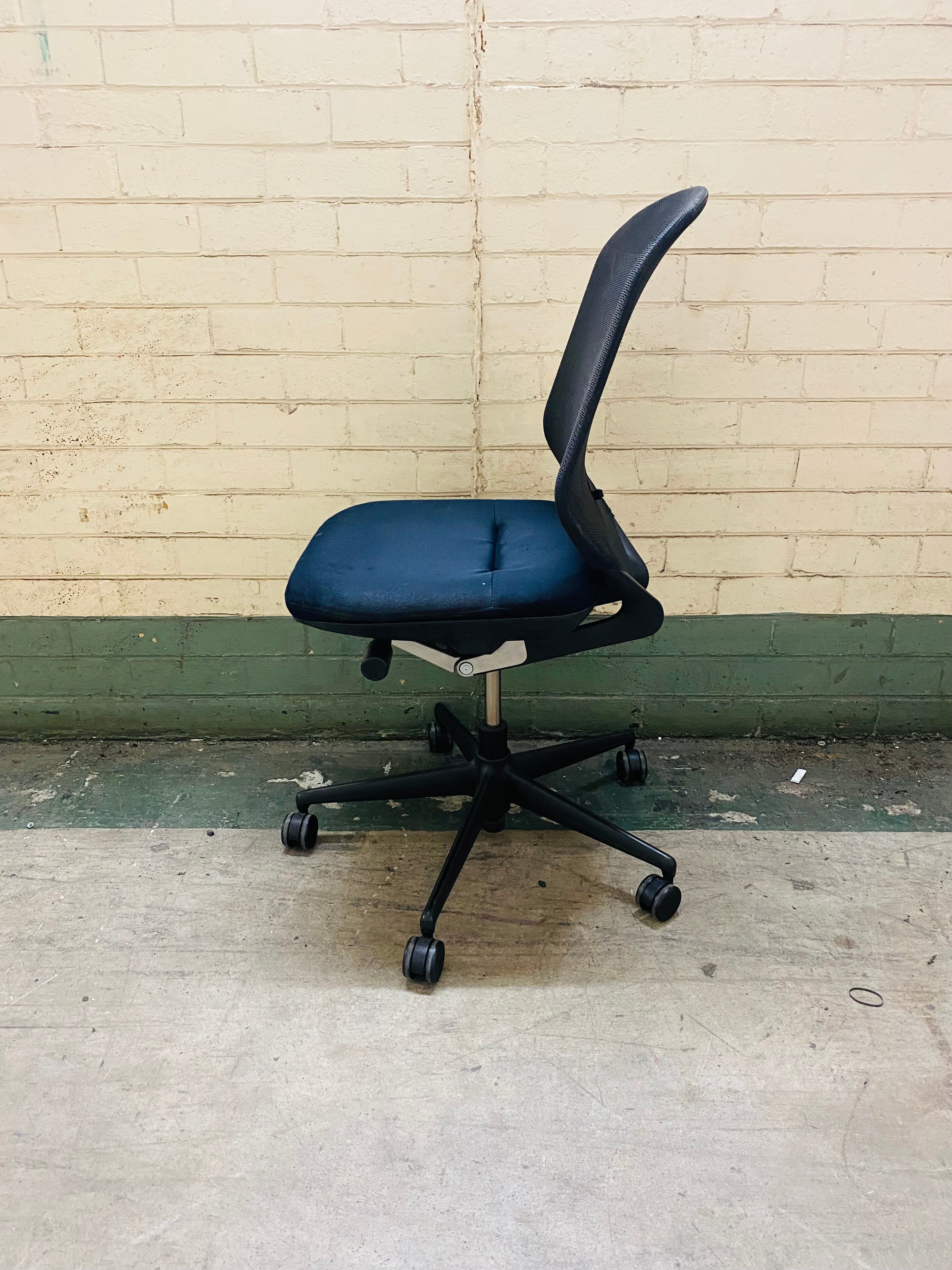 Black office chair with blue seat against a beige brick wall.