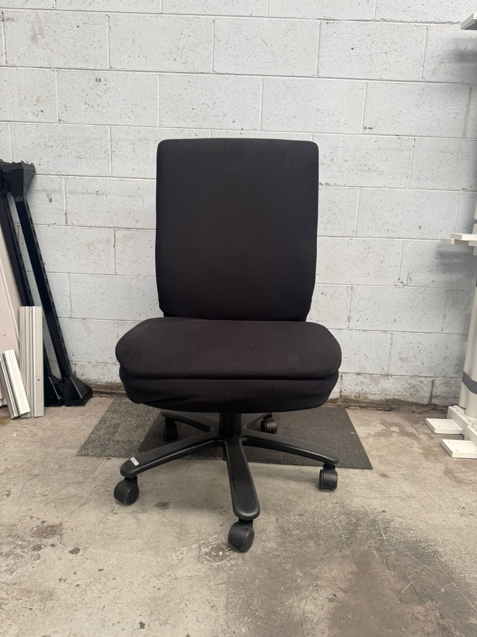 Black office chair in a room with a concrete floor and white tiled wall.