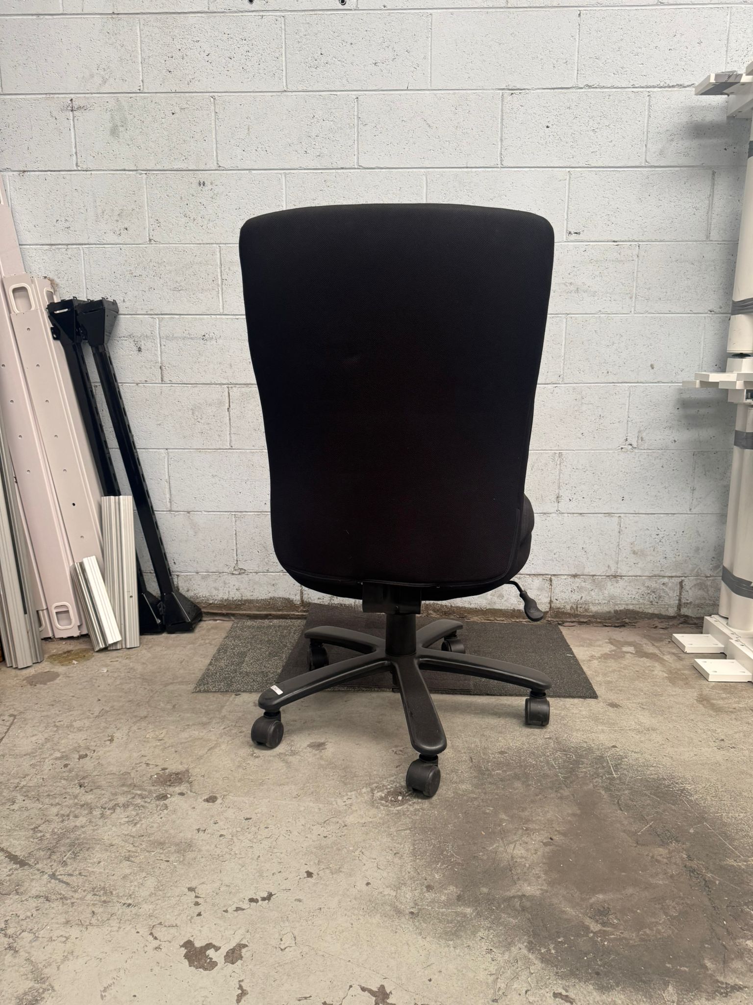 Black office chair in a room with a concrete floor and white brick wall.