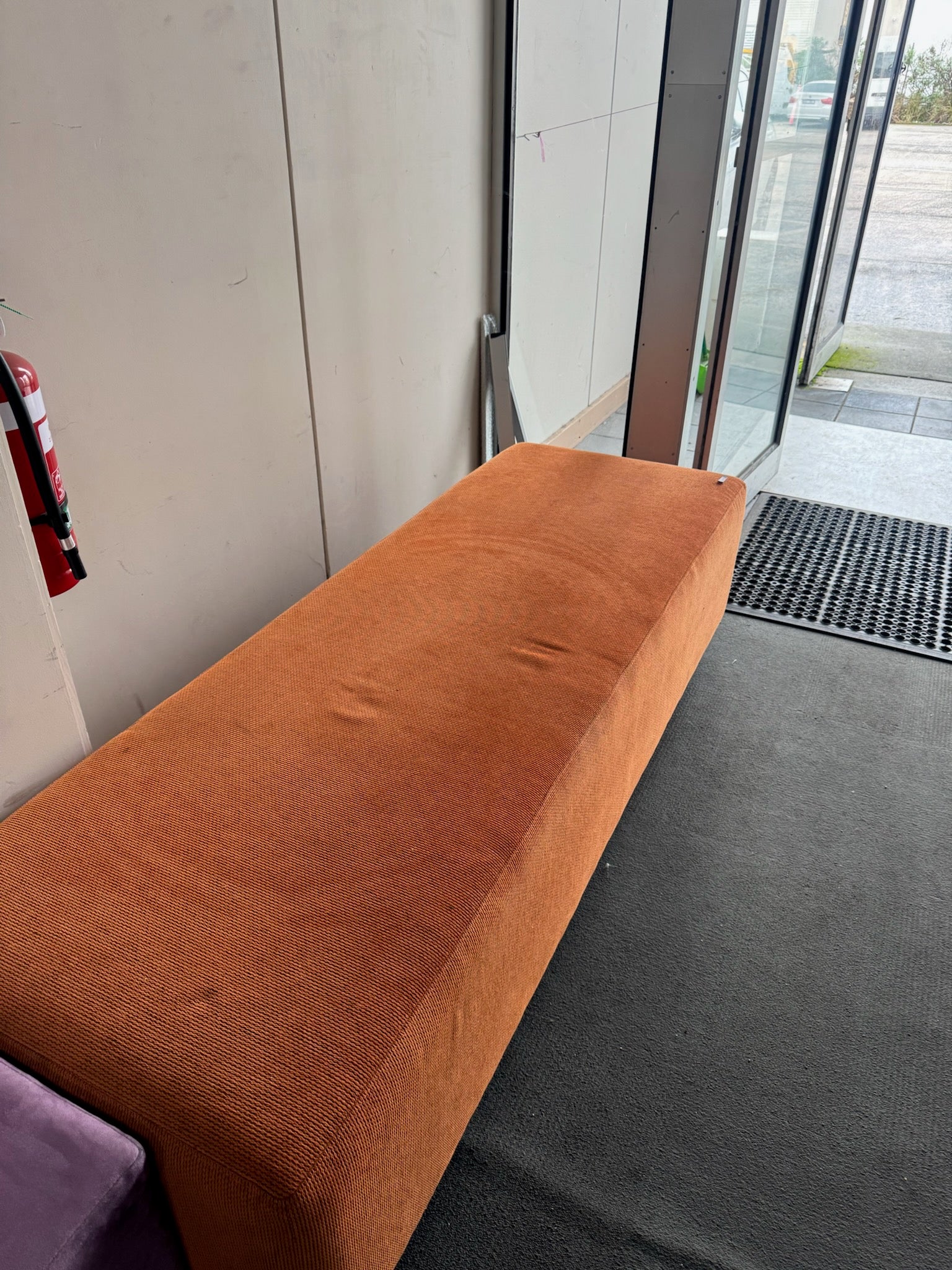 Brown bench against a wall with a glass door in the background