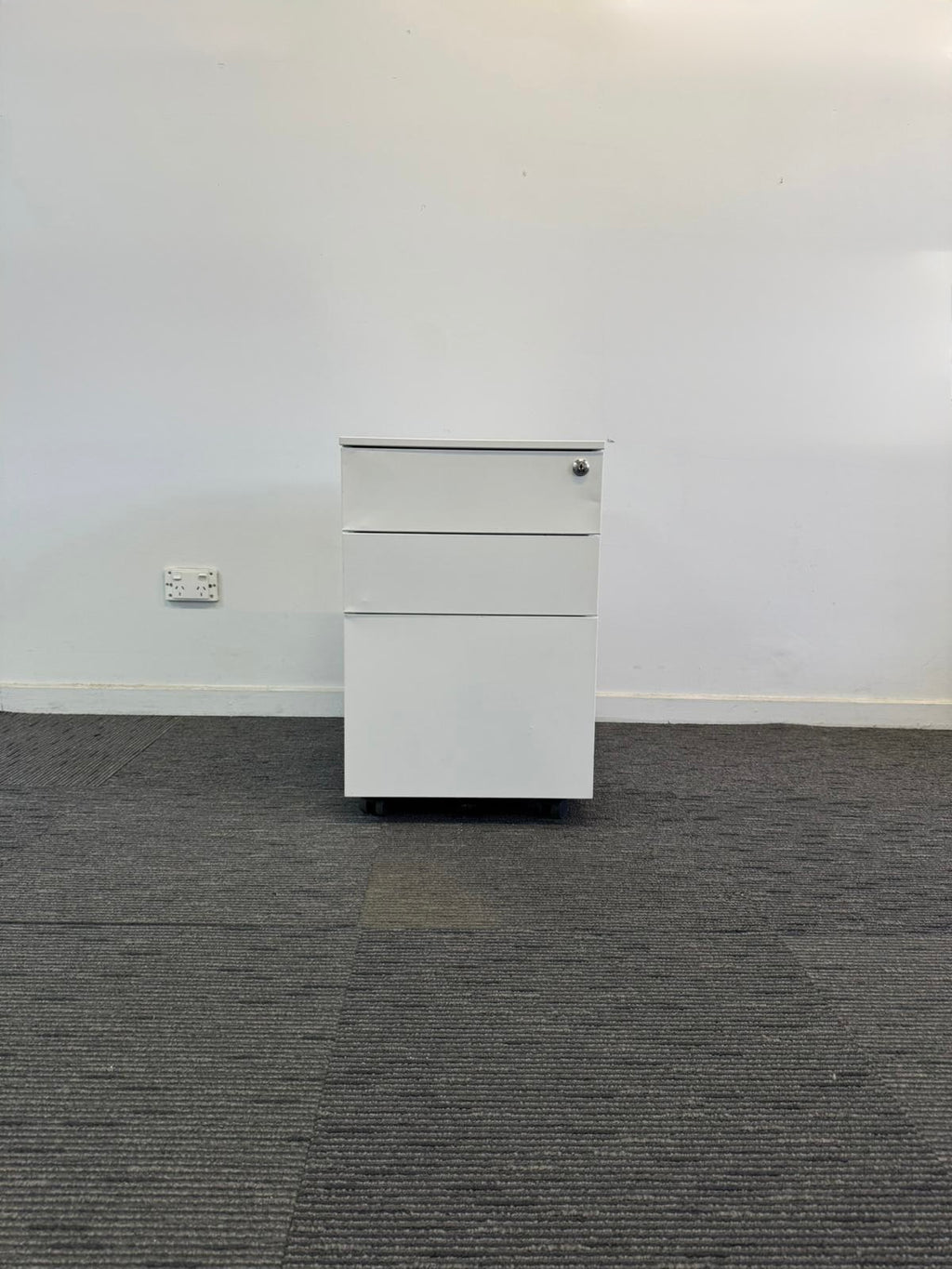 White filing cabinet against a white wall on a gray carpeted floor