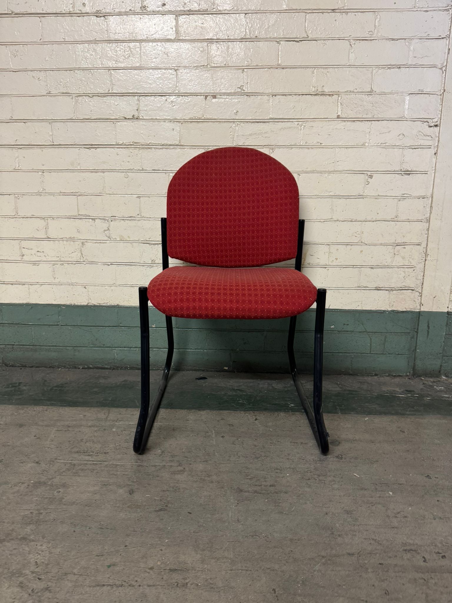 Red chair with black frame against a white brick wall.