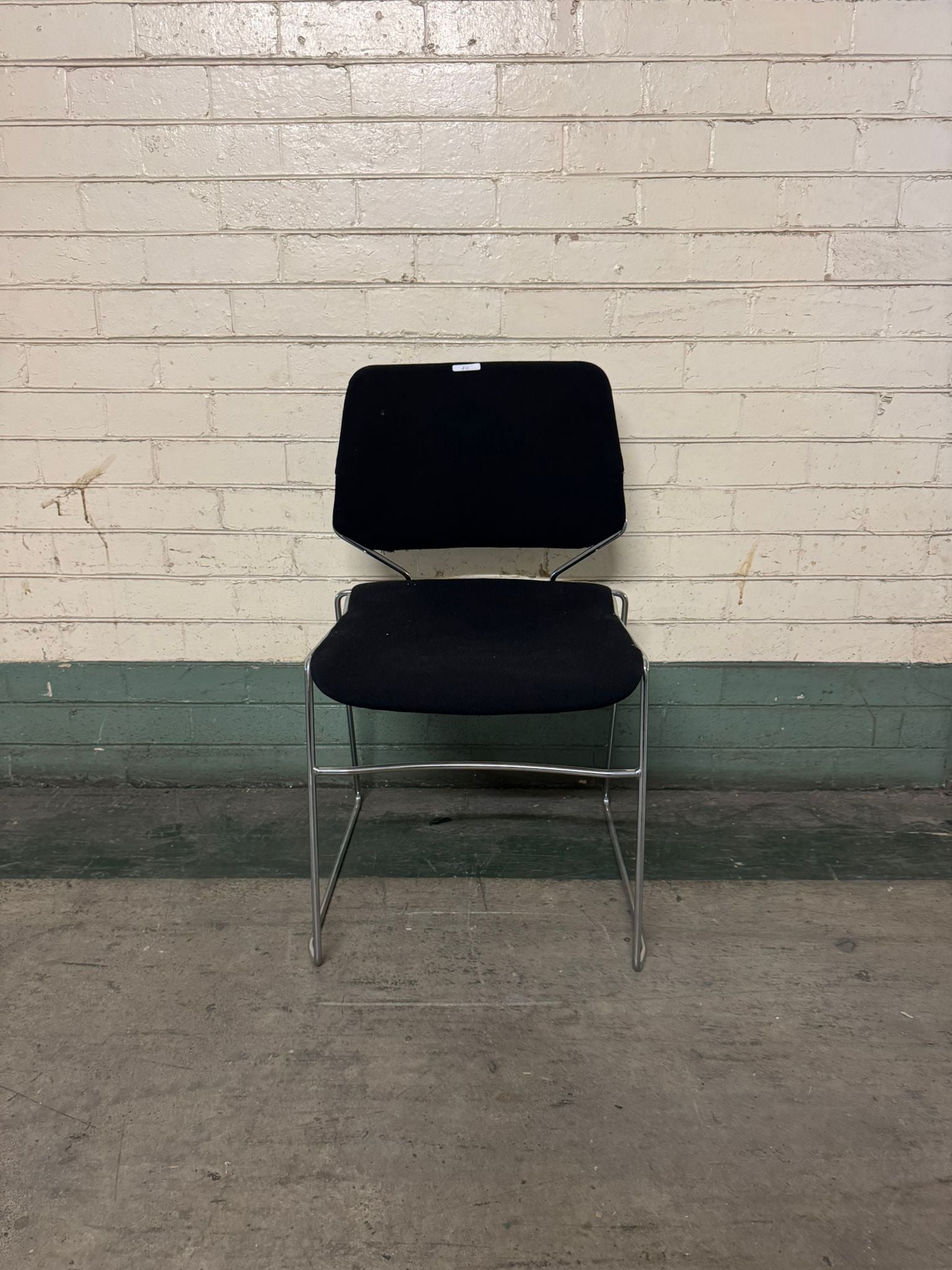 Black chair with a metal frame against a white brick wall.