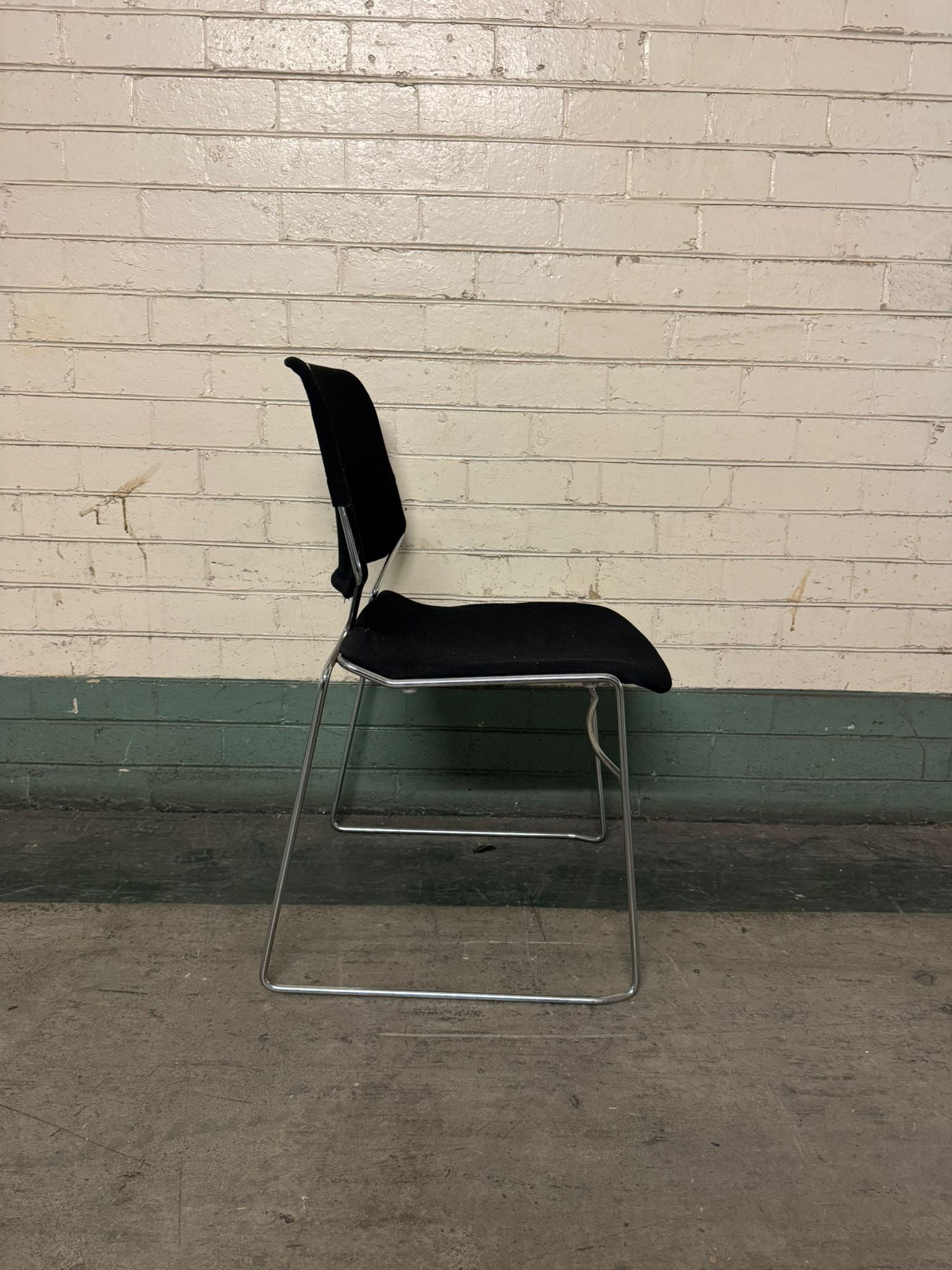 Black chair with metal legs against a white brick wall.