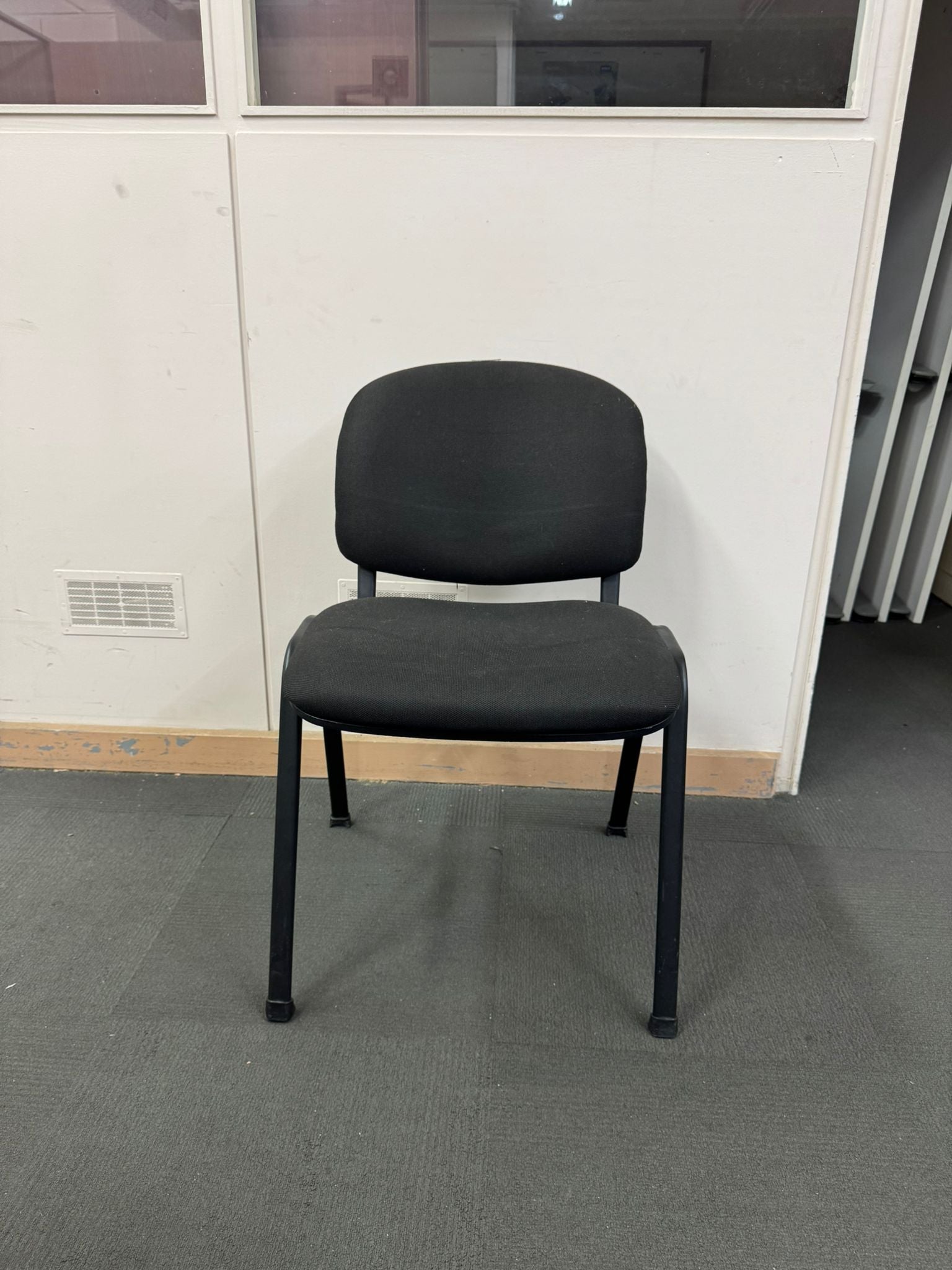 Black chair in a room with a white wall and gray floor.