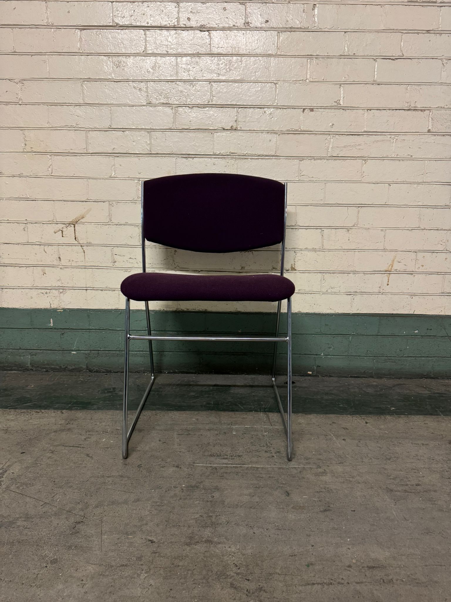 Chair with purple seat and backrest against a brick wall.