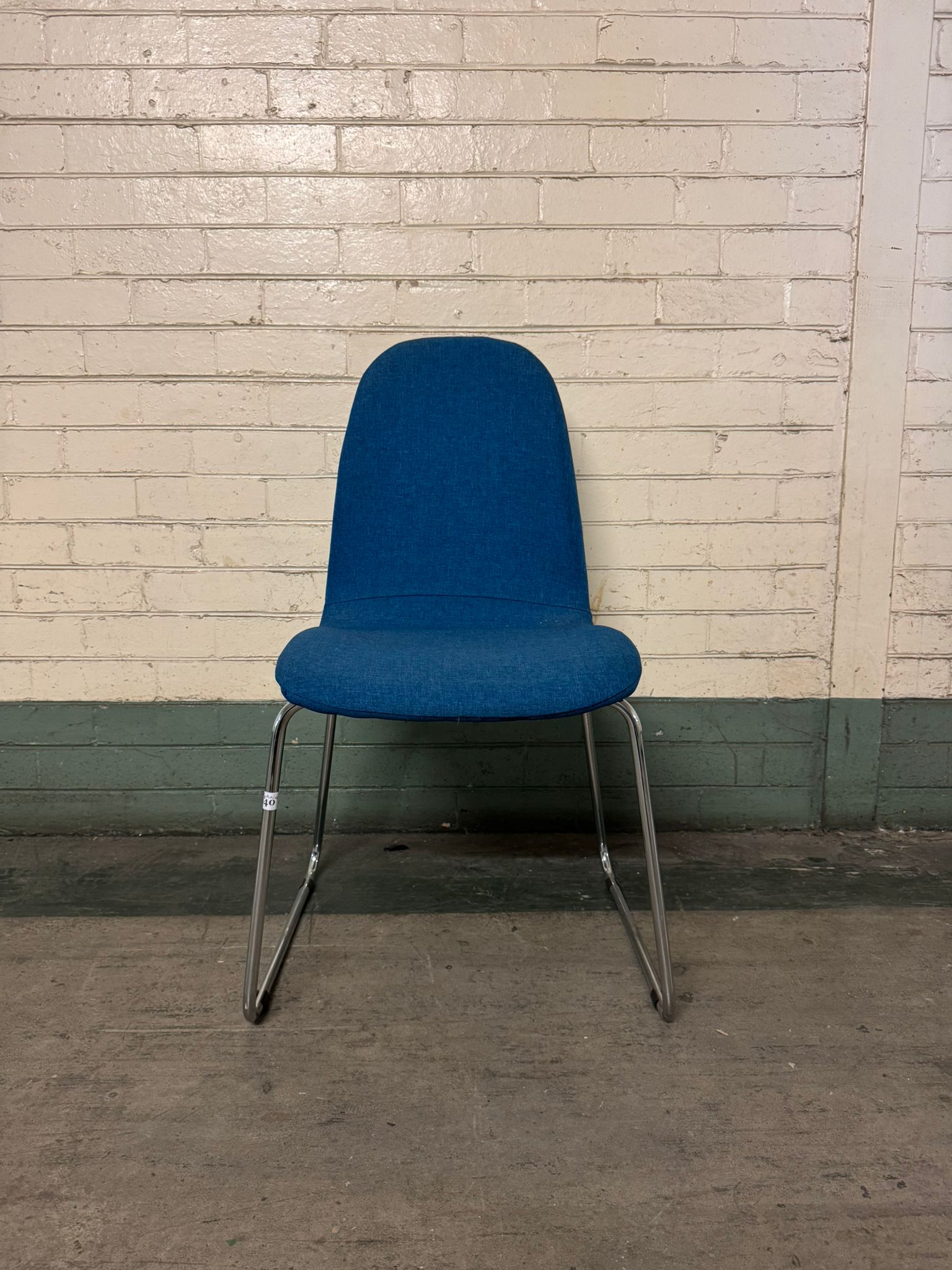 Blue chair with metal legs against a brick wall.
