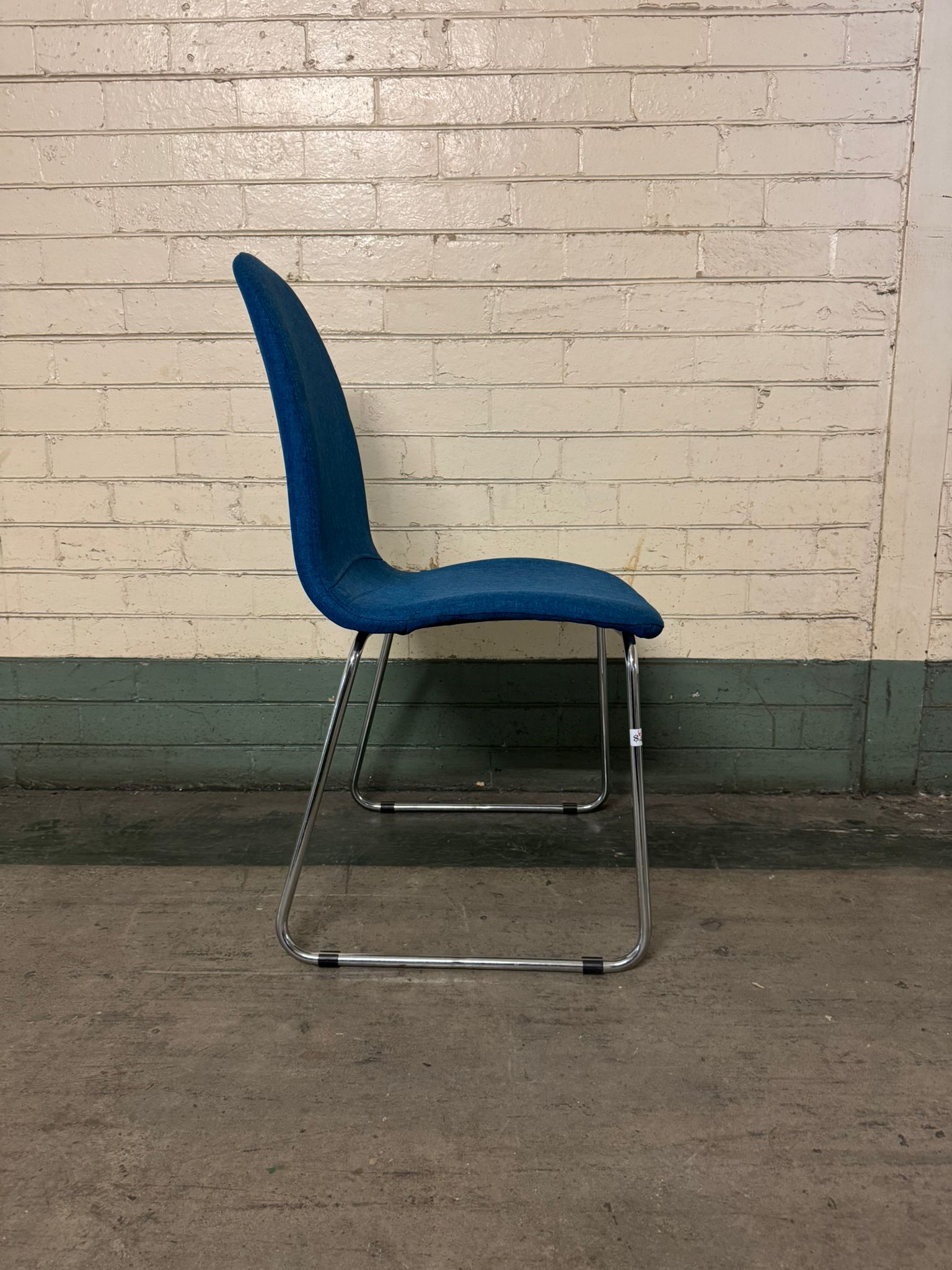 Blue chair with chrome legs against a brick wall.