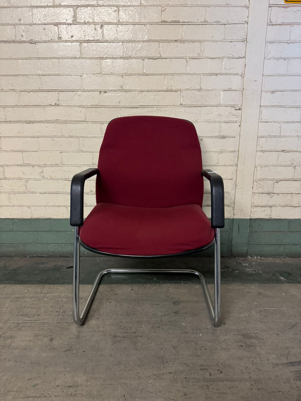 Red chair with black armrests against a brick wall.