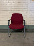 Red chair with black armrests against a brick wall.