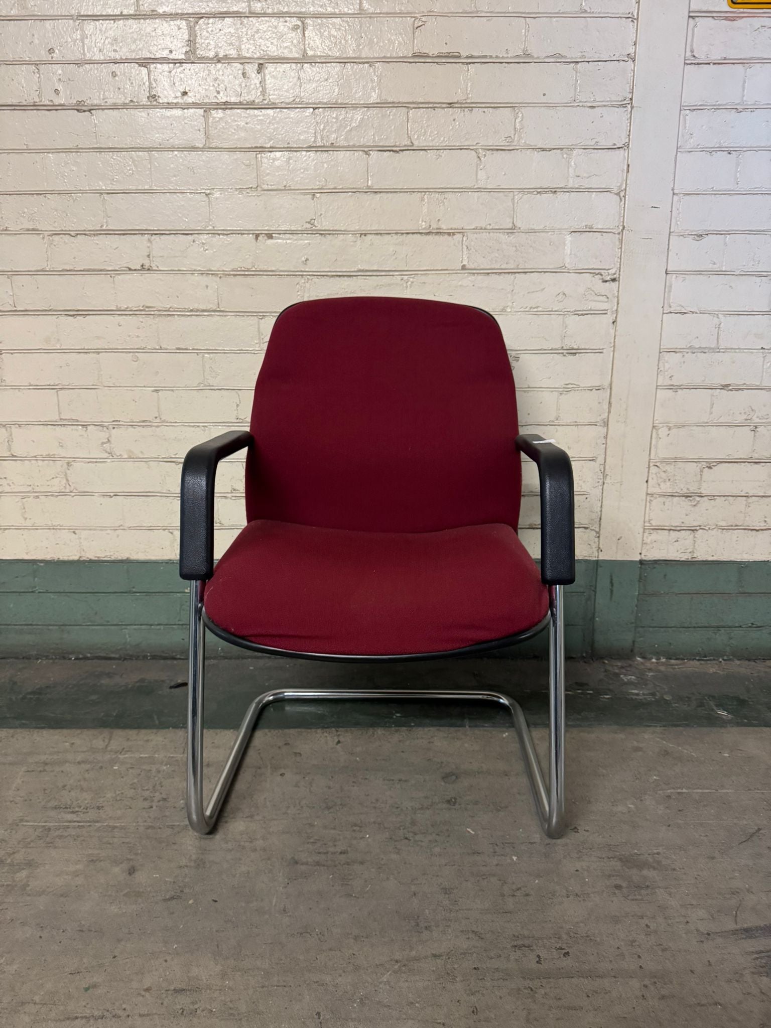 Red chair with black armrests against a brick wall.