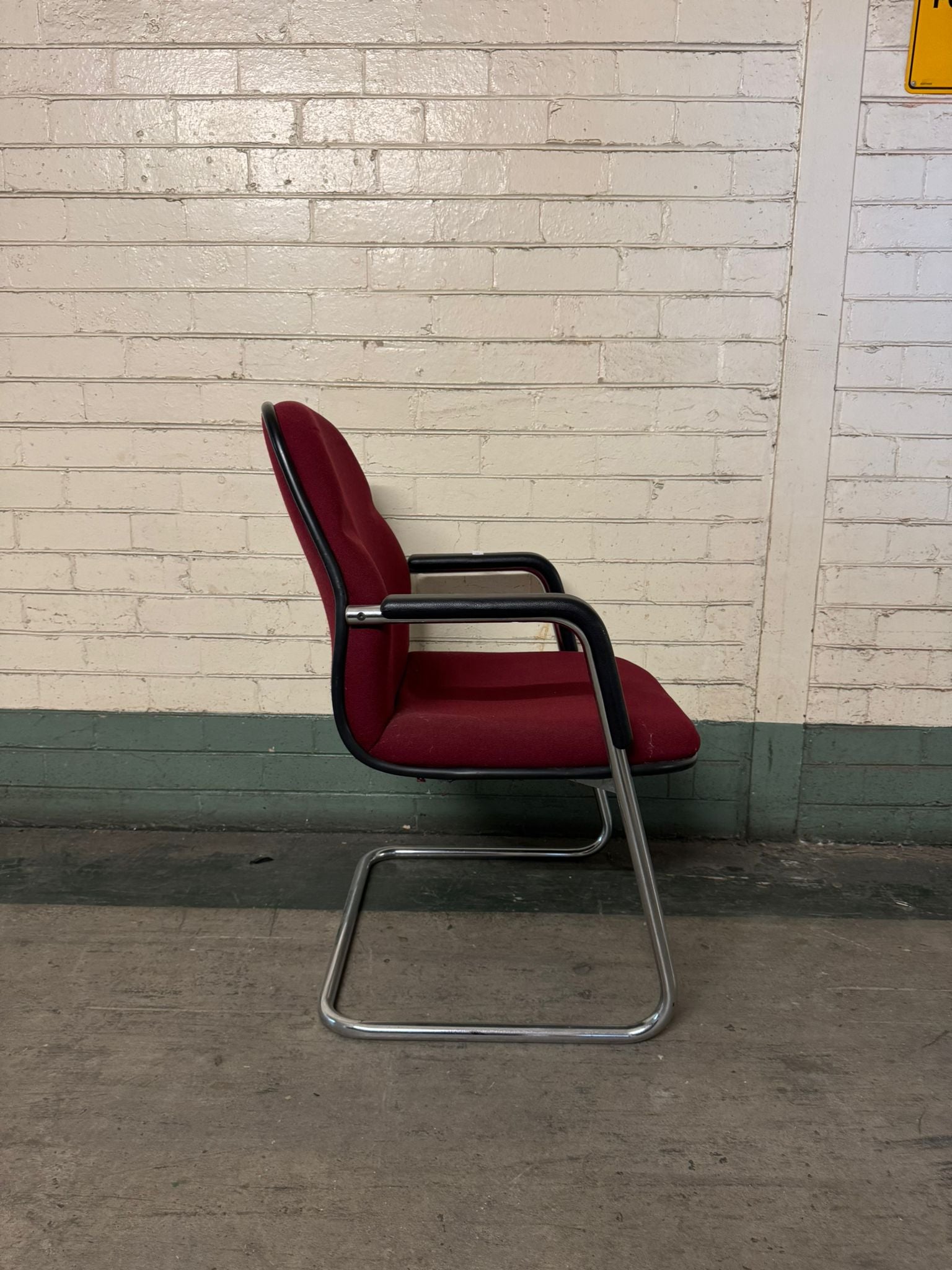 Red office chair with a metal frame against a light brick wall.