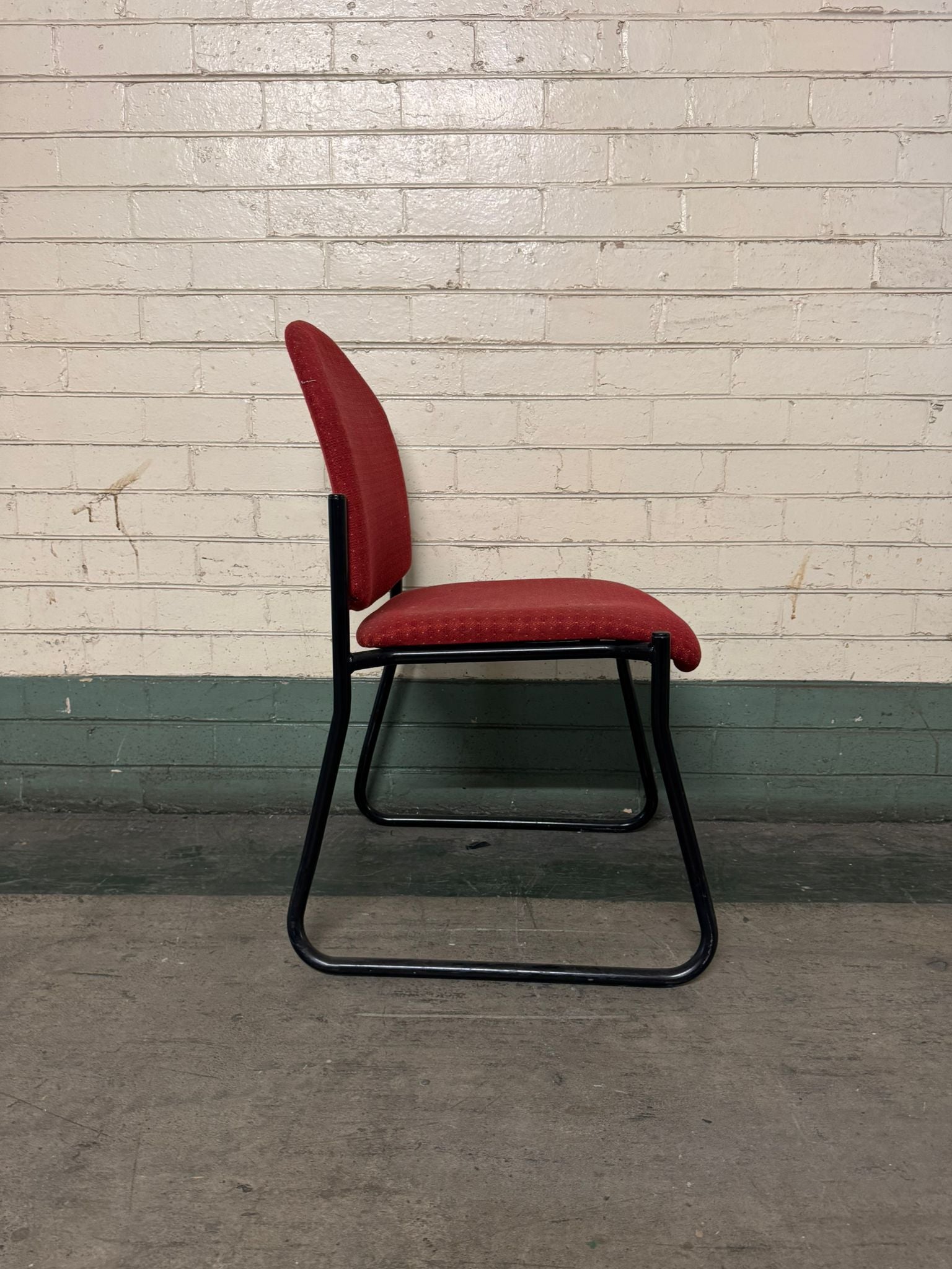 Red chair with black frame against a brick wall.